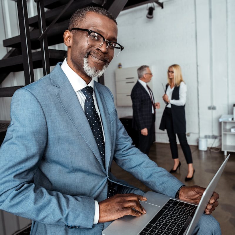 selective focus of happy african american man using laptop near partners in office