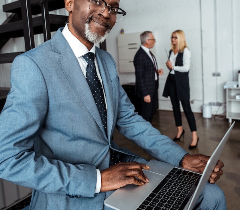 selective focus of happy african american man using laptop near partners in office